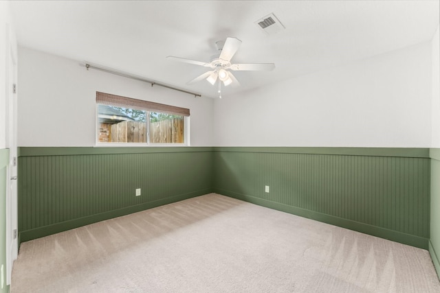 carpeted spare room with a ceiling fan, visible vents, and wainscoting