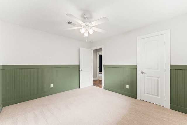 unfurnished bedroom with visible vents, carpet, wainscoting, and a ceiling fan
