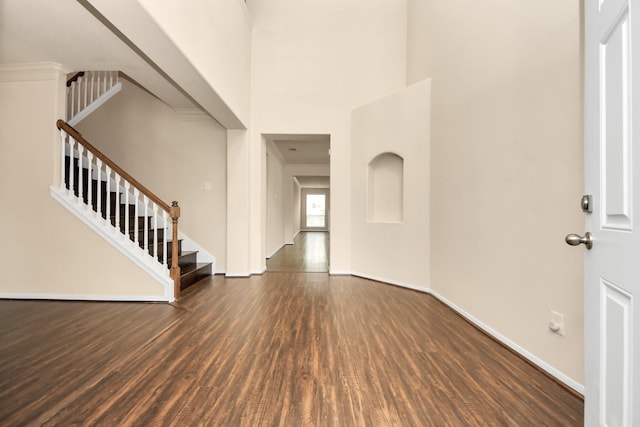 foyer entrance featuring a high ceiling, baseboards, wood finished floors, and stairway