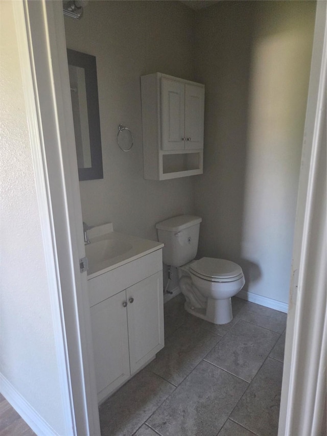 bathroom with toilet, tile patterned floors, baseboards, and vanity