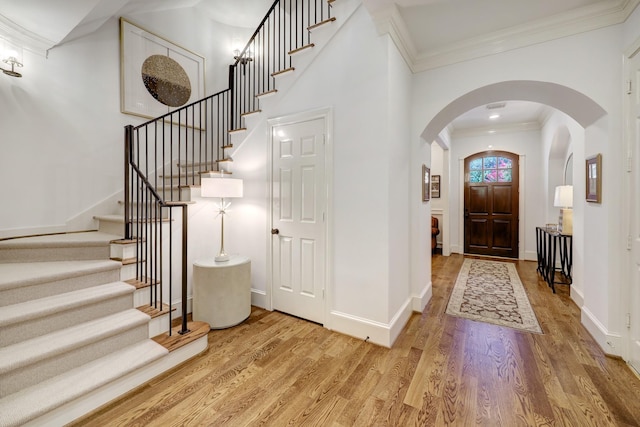 entryway with crown molding, arched walkways, stairs, baseboards, and light wood-type flooring