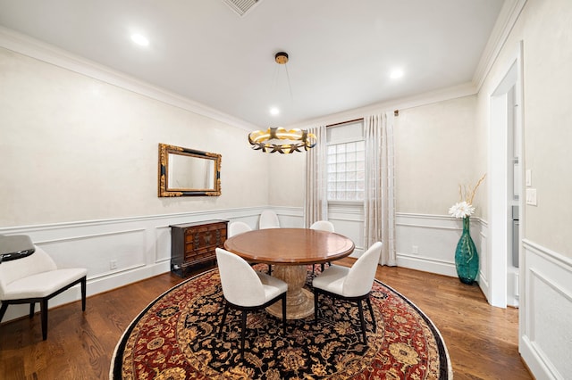 dining room featuring crown molding, an inviting chandelier, wainscoting, a decorative wall, and wood finished floors