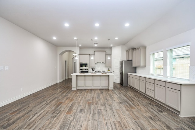 kitchen with arched walkways, wood finished floors, gray cabinetry, light countertops, and stainless steel appliances