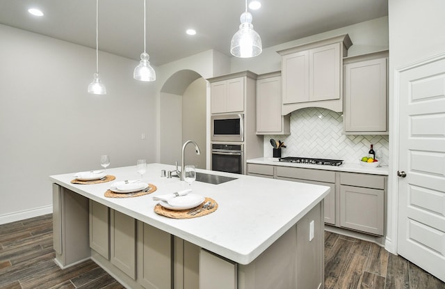 kitchen with gas cooktop, a sink, stainless steel oven, gray cabinetry, and a center island with sink