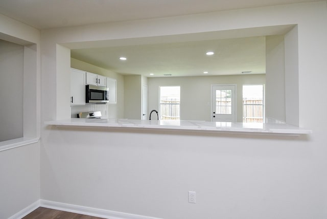 kitchen with a peninsula, recessed lighting, white cabinetry, stainless steel microwave, and dark wood finished floors