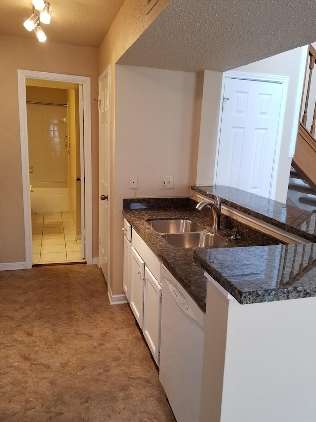 kitchen with white dishwasher, a textured ceiling, white cabinetry, a sink, and dark stone countertops