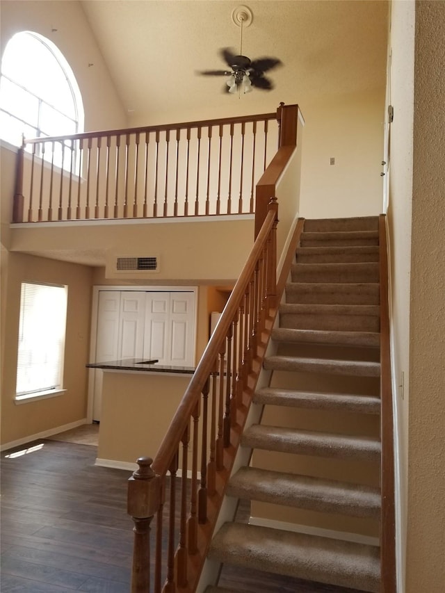 stairway featuring a ceiling fan, visible vents, wood finished floors, high vaulted ceiling, and baseboards