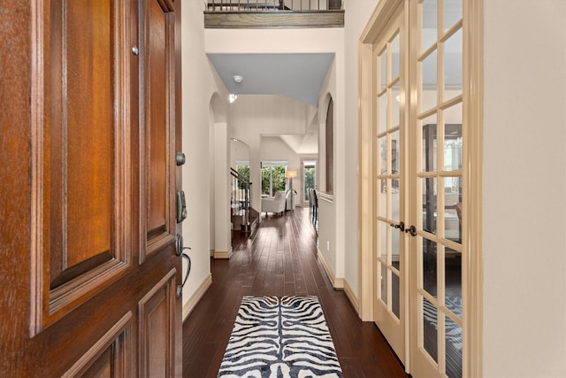 hallway featuring arched walkways, baseboards, french doors, and dark wood-type flooring