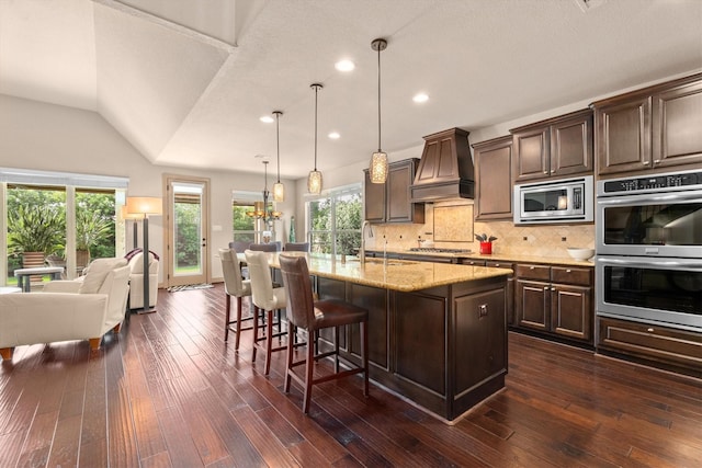 kitchen with decorative backsplash, dark brown cabinetry, appliances with stainless steel finishes, a sink, and premium range hood