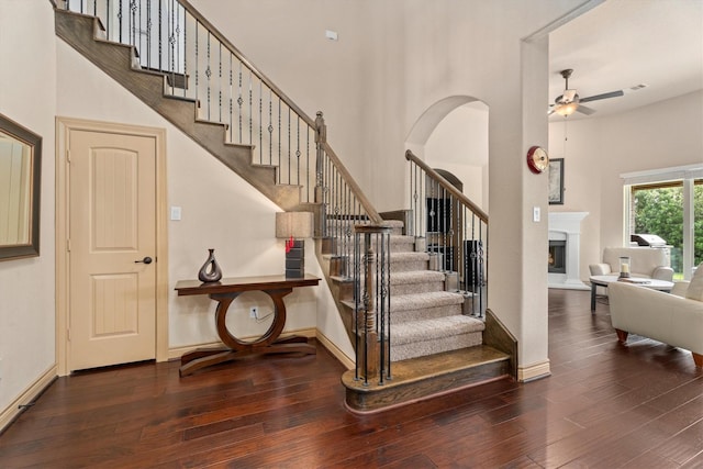 stairway featuring baseboards, wood-type flooring, a ceiling fan, and a towering ceiling