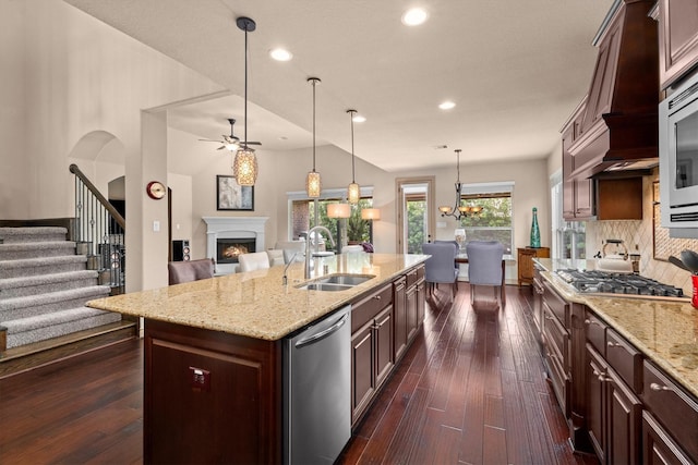 kitchen featuring stainless steel appliances, open floor plan, a lit fireplace, and a sink