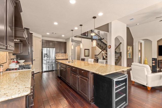kitchen with dark brown cabinetry, open floor plan, stainless steel refrigerator with ice dispenser, arched walkways, and a sink