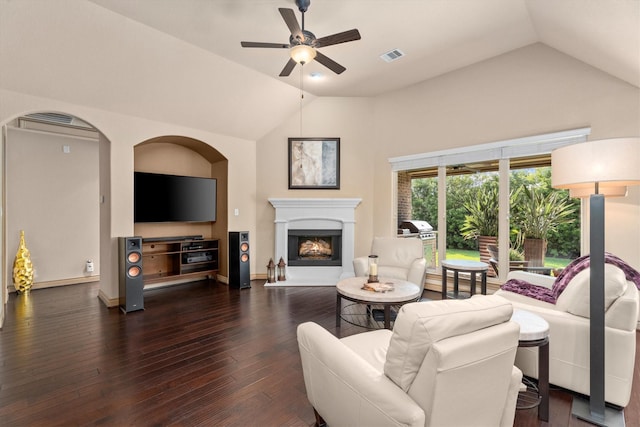 living room with a warm lit fireplace, visible vents, a ceiling fan, vaulted ceiling, and dark wood-style floors