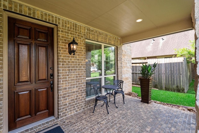 doorway to property featuring a porch, brick siding, and fence