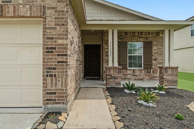 doorway to property featuring brick siding, an attached garage, and a porch