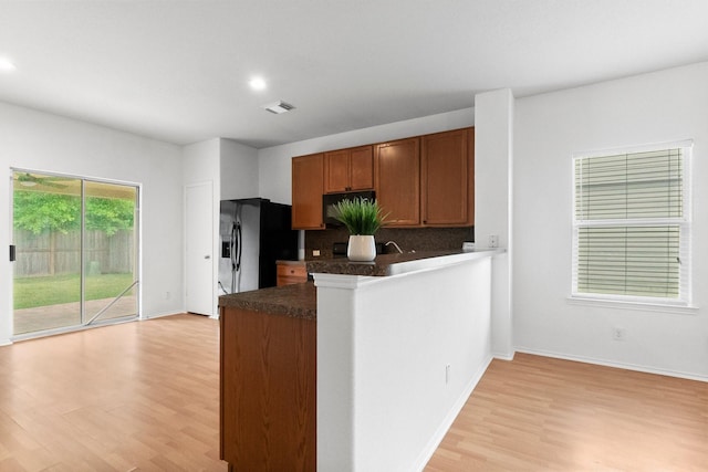 kitchen featuring dark countertops, stainless steel fridge, light wood-style floors, brown cabinetry, and tasteful backsplash