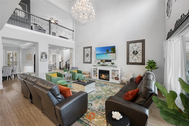 living area with a high ceiling, a notable chandelier, a glass covered fireplace, and stairway