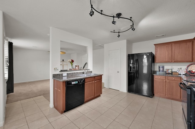 kitchen with black appliances, a sink, brown cabinetry, and dark stone counters