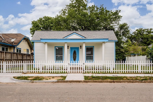 bungalow-style home with a porch, a fenced front yard, and roof with shingles