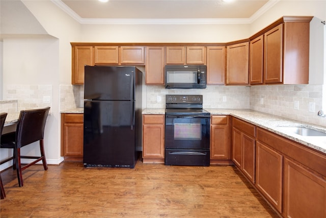 kitchen featuring crown molding, light stone countertops, black appliances, and light wood finished floors