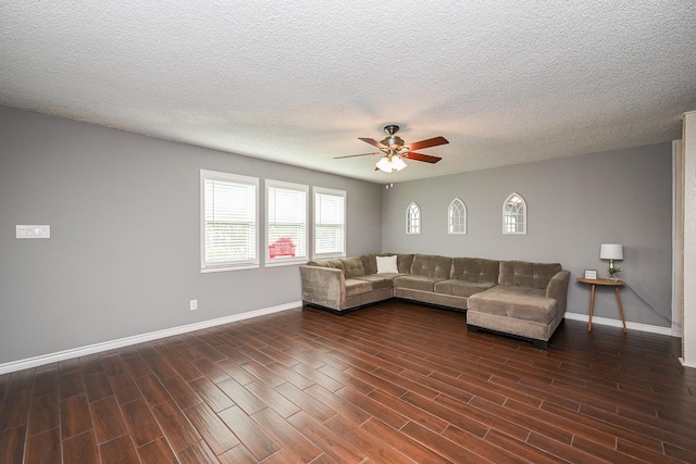 living area featuring baseboards, a ceiling fan, a textured ceiling, and dark wood-type flooring