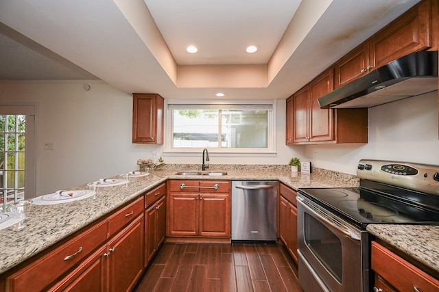 kitchen with light stone countertops, dark wood-style floors, under cabinet range hood, a sink, and appliances with stainless steel finishes