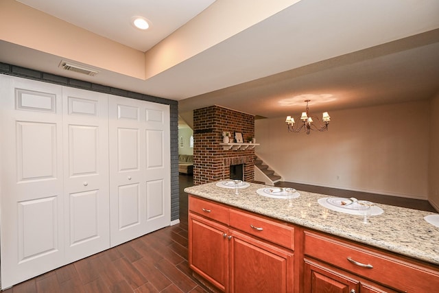 kitchen featuring dark wood-style flooring, light stone countertops, a notable chandelier, a brick fireplace, and visible vents