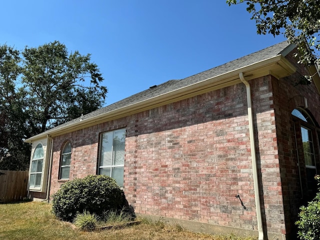 view of home's exterior with brick siding, roof with shingles, and fence