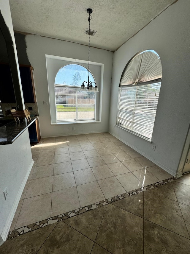 unfurnished dining area featuring a textured ceiling, visible vents, baseboards, a chandelier, and light tile patterned flooring