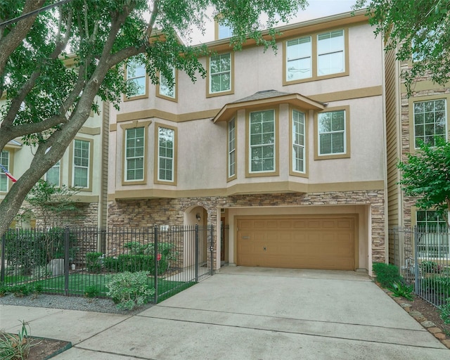 townhome / multi-family property with a garage, driveway, stone siding, and stucco siding