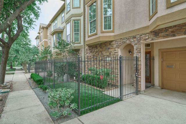 view of side of home with a fenced front yard, a gate, stone siding, and stucco siding