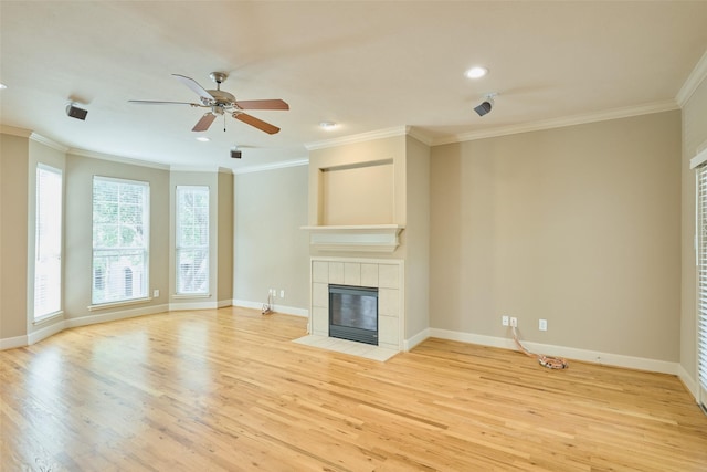 unfurnished living room with a tiled fireplace, crown molding, light wood-style flooring, and ceiling fan