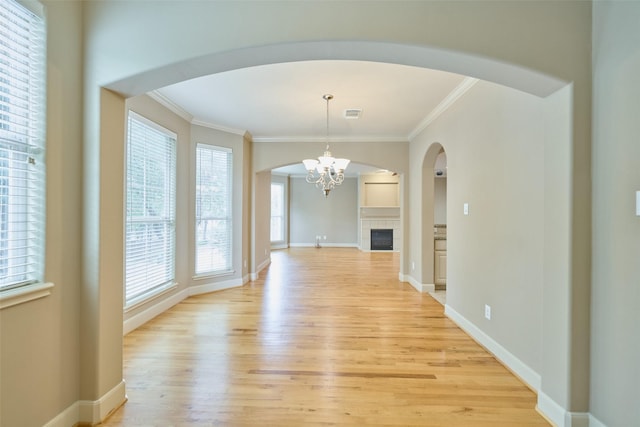 unfurnished dining area featuring crown molding, light wood-style flooring, a chandelier, and a tile fireplace