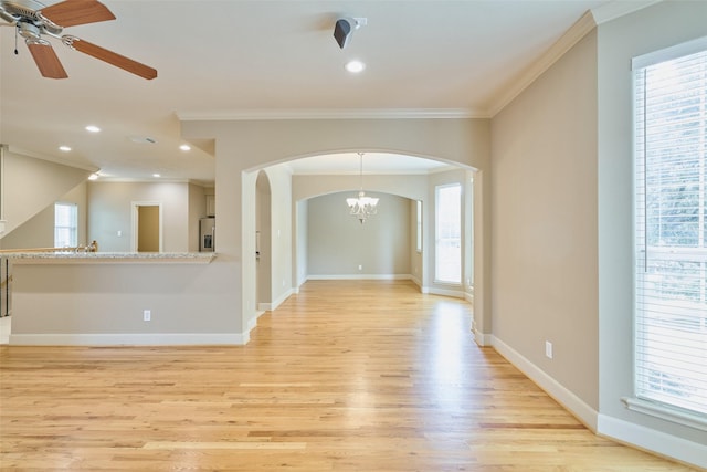 unfurnished room with arched walkways, light wood finished floors, ceiling fan with notable chandelier, and ornamental molding