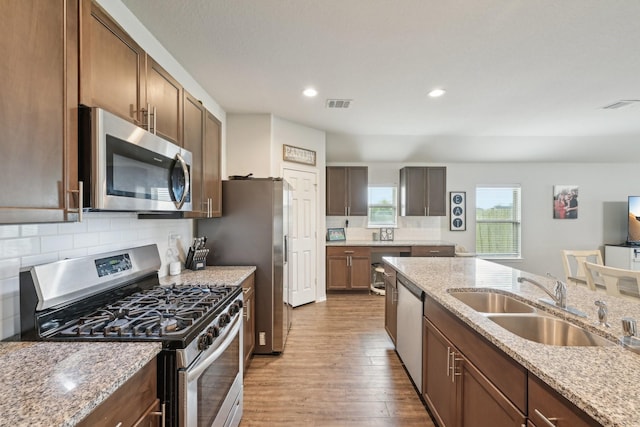 kitchen with a sink, stainless steel appliances, wood finished floors, tasteful backsplash, and visible vents