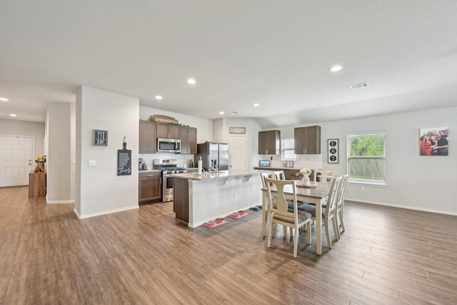 kitchen with a kitchen island with sink, visible vents, wood finished floors, light countertops, and stainless steel appliances