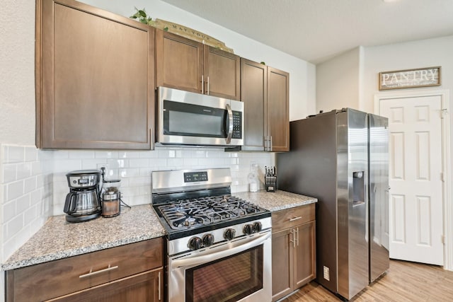 kitchen featuring backsplash, stainless steel appliances, light stone countertops, and light wood-type flooring