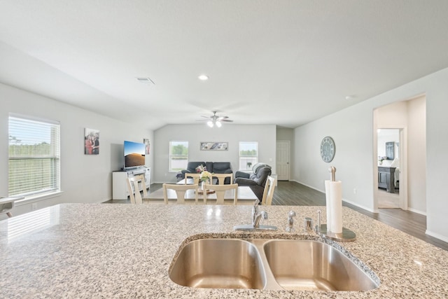 kitchen with visible vents, a ceiling fan, open floor plan, light stone counters, and a sink
