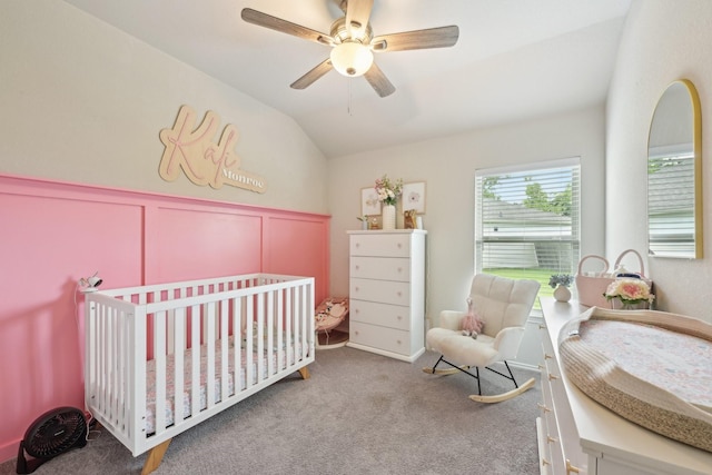 carpeted bedroom with a nursery area, wainscoting, a decorative wall, a ceiling fan, and vaulted ceiling