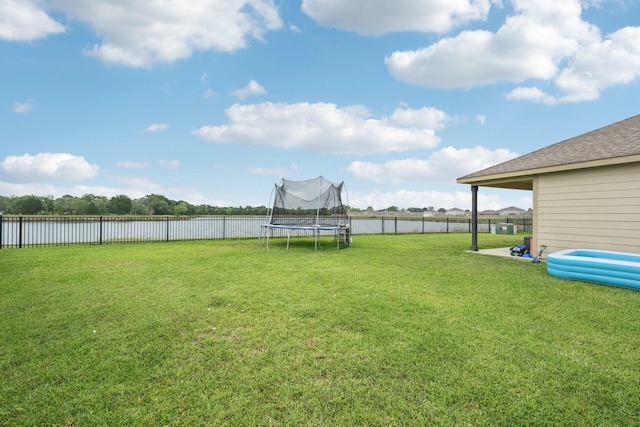 view of yard with a fenced backyard, a trampoline, and a water view