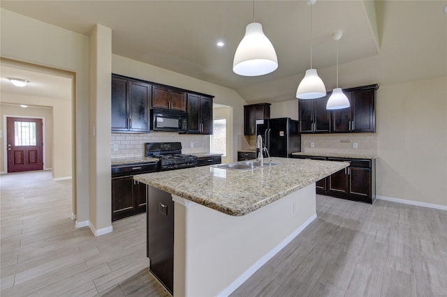 kitchen featuring a kitchen island with sink, dark brown cabinets, tasteful backsplash, a sink, and black appliances
