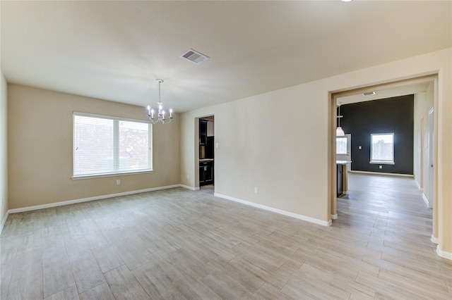 spare room featuring a healthy amount of sunlight, visible vents, light wood finished floors, and a notable chandelier