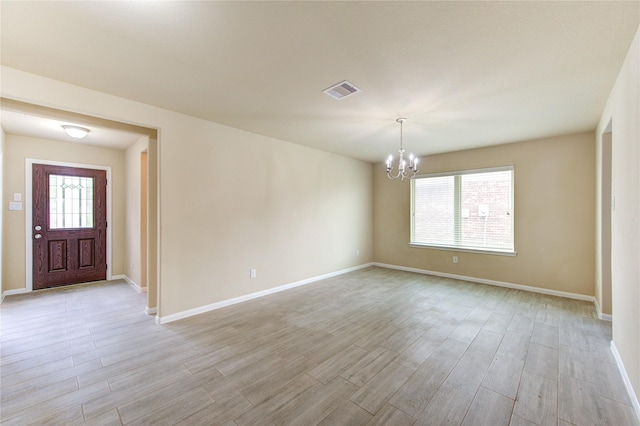 spare room featuring an inviting chandelier, baseboards, visible vents, and light wood-type flooring