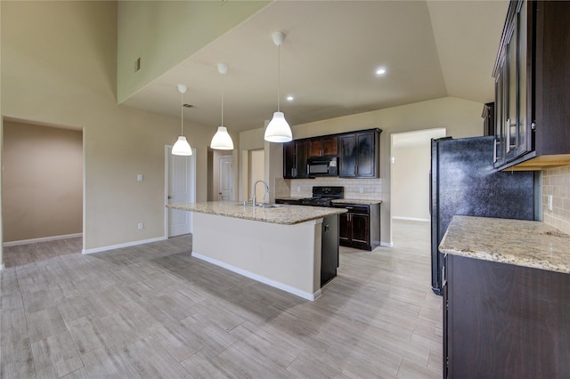 kitchen featuring an island with sink, light stone counters, a sink, backsplash, and black appliances