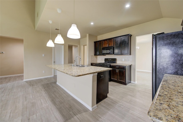 kitchen featuring dark brown cabinets, a sink, an island with sink, tasteful backsplash, and black appliances