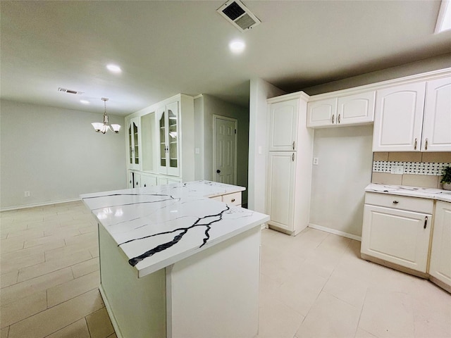 kitchen with a kitchen island, white cabinetry, a chandelier, and visible vents