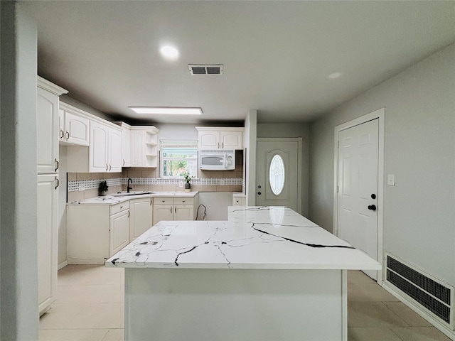 kitchen with visible vents, a sink, open shelves, and white microwave