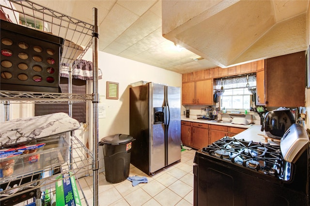 kitchen with brown cabinetry, black range with gas stovetop, stainless steel fridge, light countertops, and light tile patterned floors