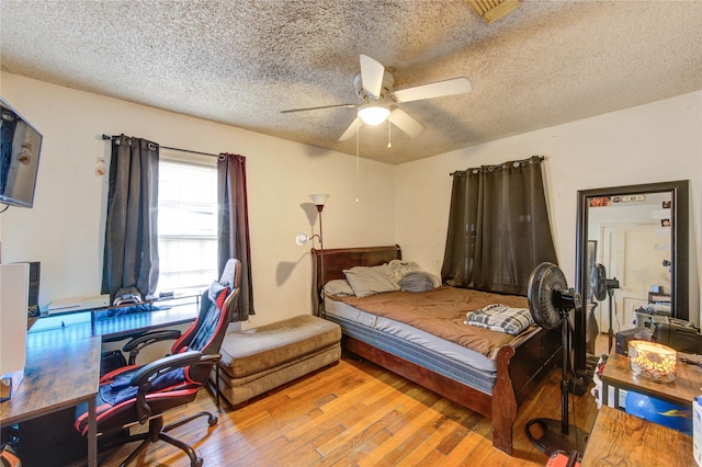 bedroom with ceiling fan, light wood finished floors, and a textured ceiling