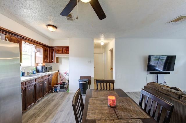 dining area with visible vents, a ceiling fan, light wood-style flooring, and a textured ceiling
